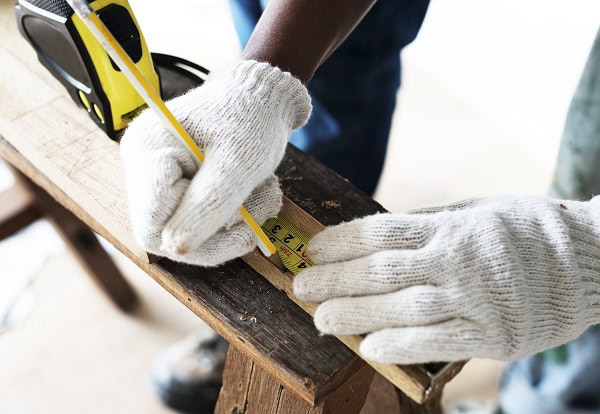 Lavori di falegnameria a Legnano Operaio edile con guanti che misura il legno durante un lavoro di ristrutturazione.